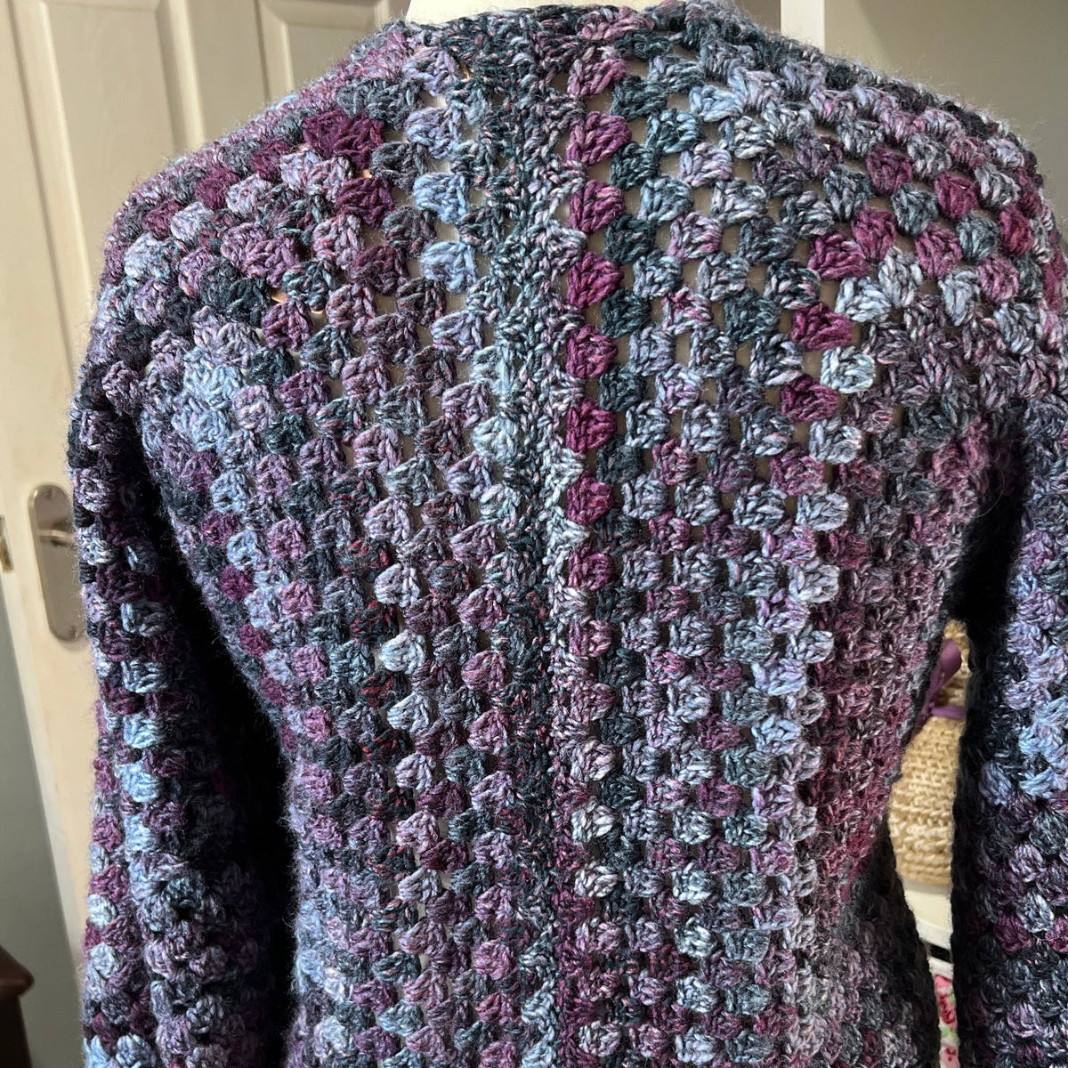 A textured, chunky knit cropped cardigan sweater with a variegated pattern of purple, blue, and gray yarn, displayed on a cream-colored dress form mannequin.